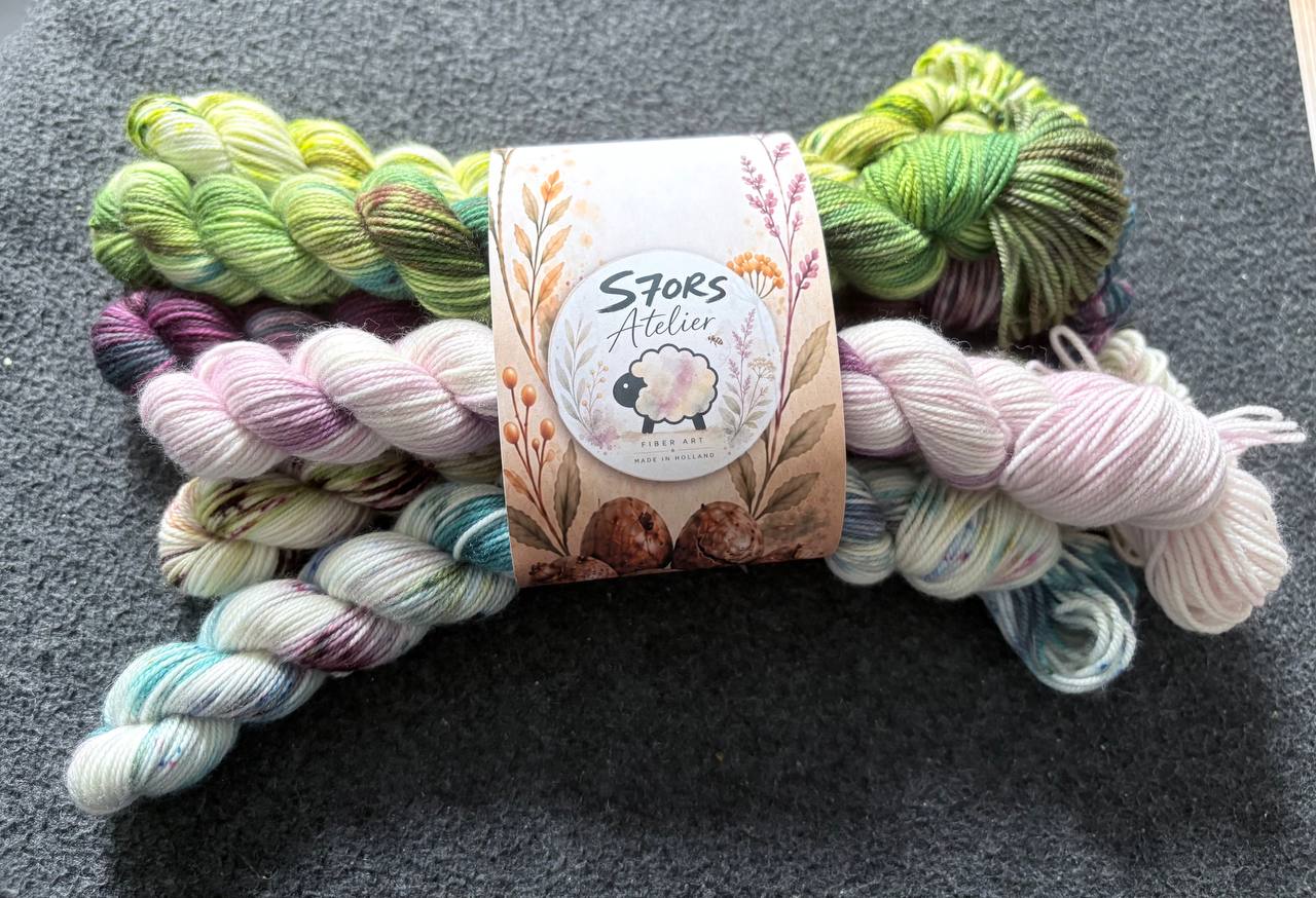 Dyed skeins of yarn in green, pink, and blue on a dark background, with an S7oRS Studio label.