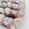 img_6a97e896fd25.jpg Light beige skeins of 4-ply yarn with S7oRS Atelier labels, photographed up close on a white background.