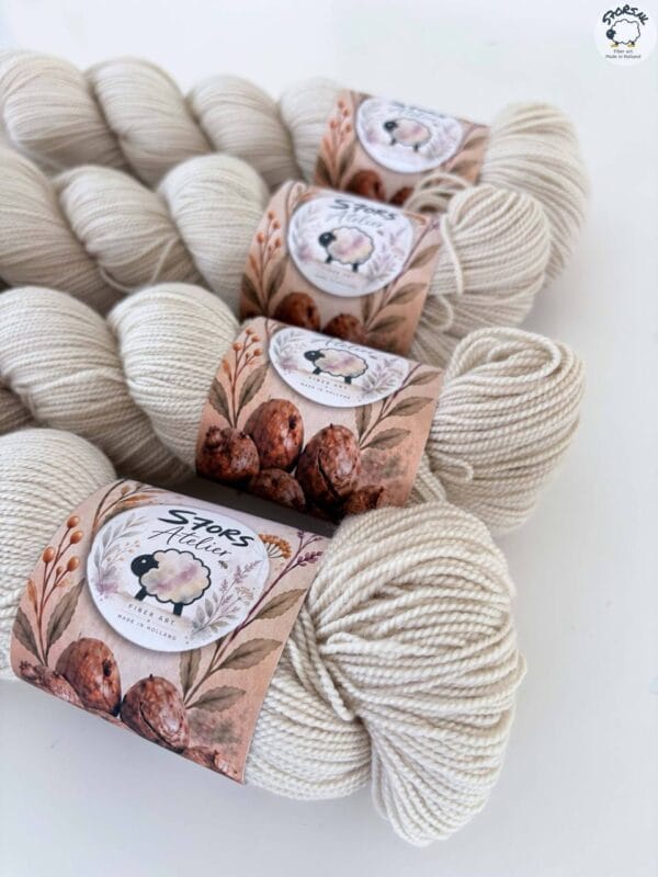 img_6a97e896fd25.jpg Light beige skeins of 4-ply yarn with S7oRS Atelier labels, photographed up close on a white background.