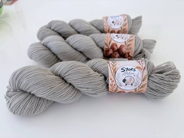img_985d0acdd3b8.jpg Leigrijze strengen 4-ply garen met S7oRS Atelier-labels op een witte ondergrond.