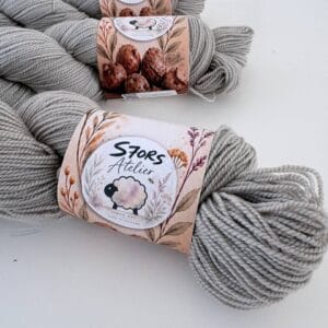 Leigrijze strengen 4-ply garen met S7oRS Atelier-labels op een witte ondergrond.