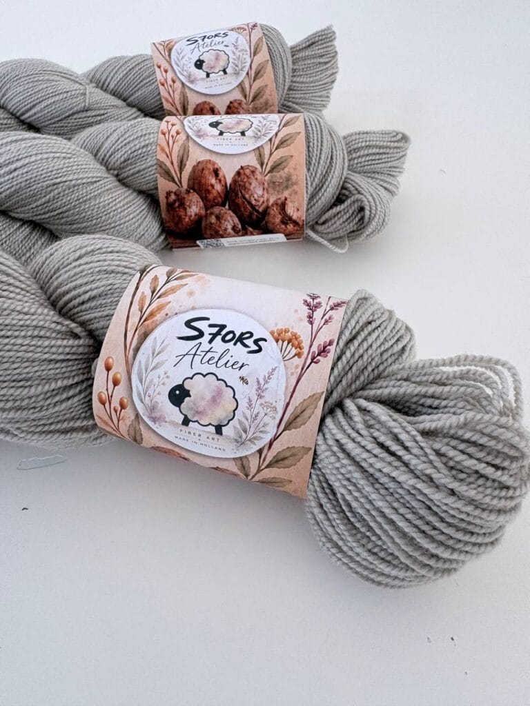 Leigrijze strengen 4-ply garen met S7oRS Atelier-labels op een witte ondergrond.