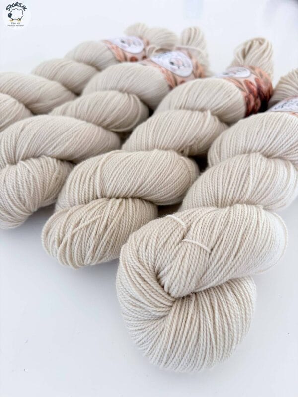 img_ba9468d94bf4.jpg Close-up of light beige, plied skeins of 4-ply yarn on a white background.