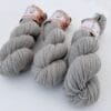 img_e119efb78c82.jpg Drie leigrijze strengen 4-ply garen met S7oRS Atelier-labels op een witte ondergrond.