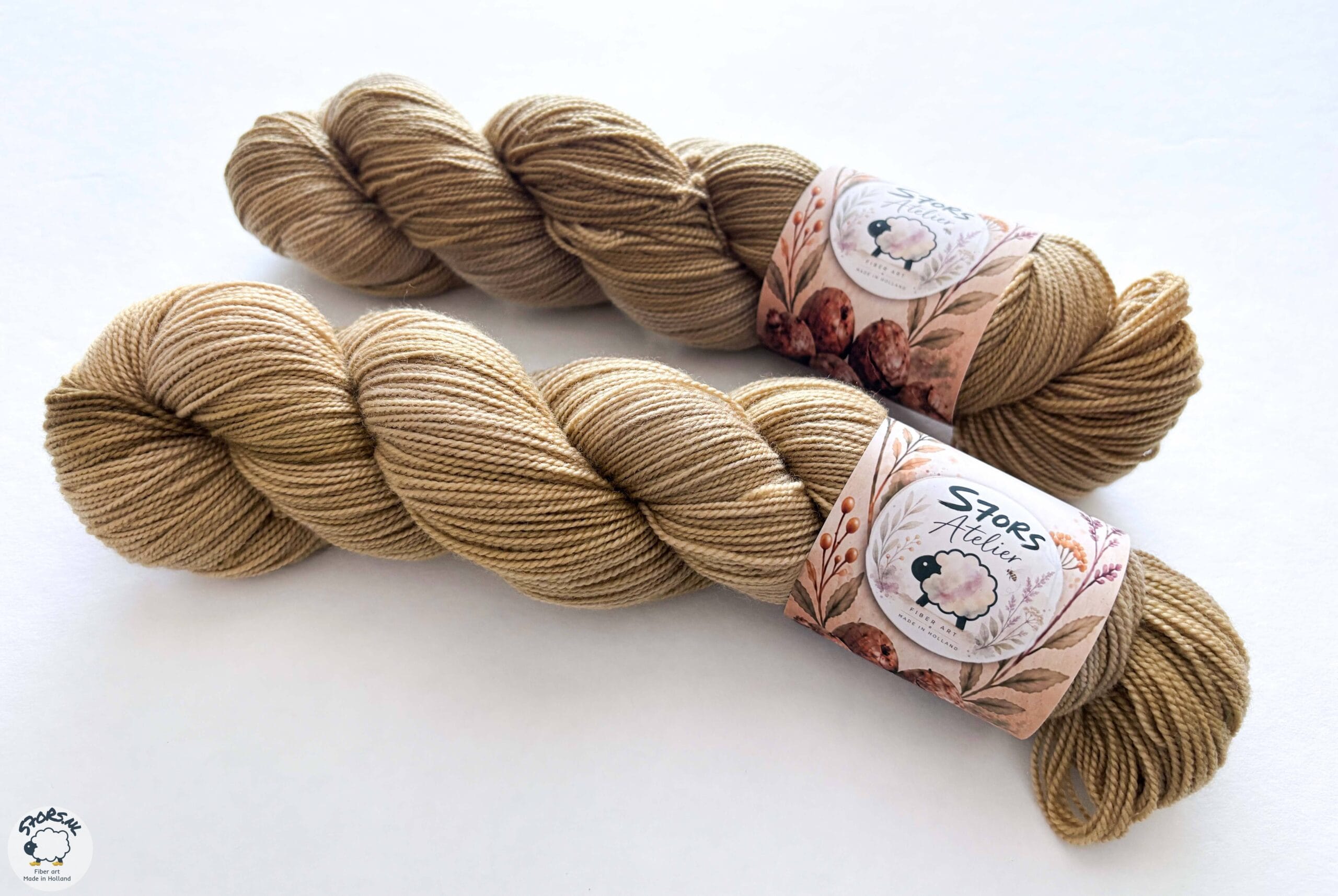Twee warmere geverfde strengen garen met S7oRS Atelier-labels op een witte ondergrond.